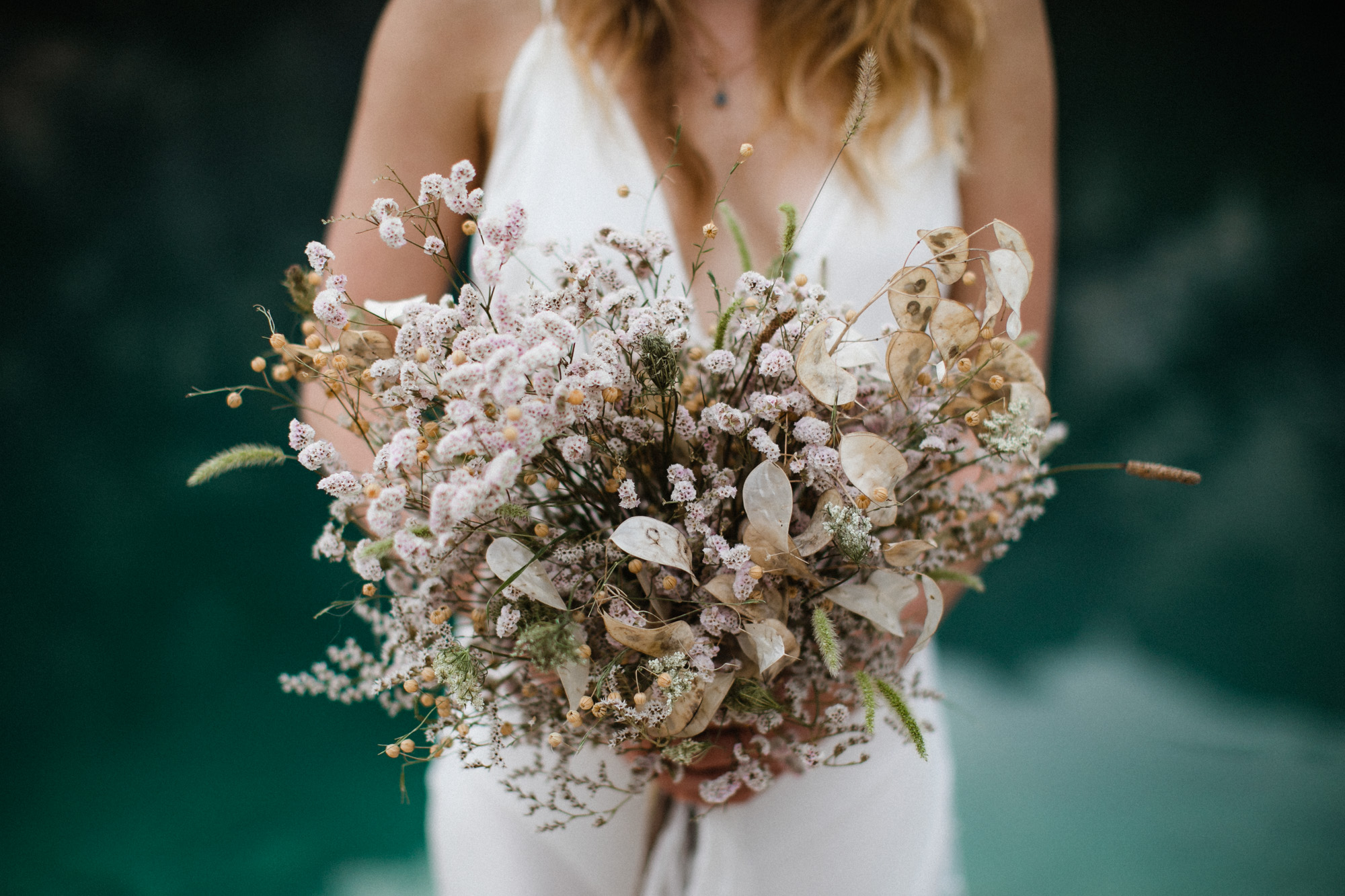 Bride holding dried bouquet at Lago di Braies in the Dolomites in Italy during elopement wedding Ana Galloway Photography