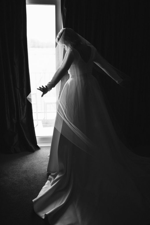 Black and White picture of bride in the window light in her bridal gown and veil Ana Galloway Photography