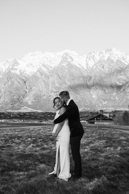 Bride and groom embracing in the evening light with the stunning Queenstown Remarkables behind them Modern Classic winter wedding at Jacks Point in Queenstown