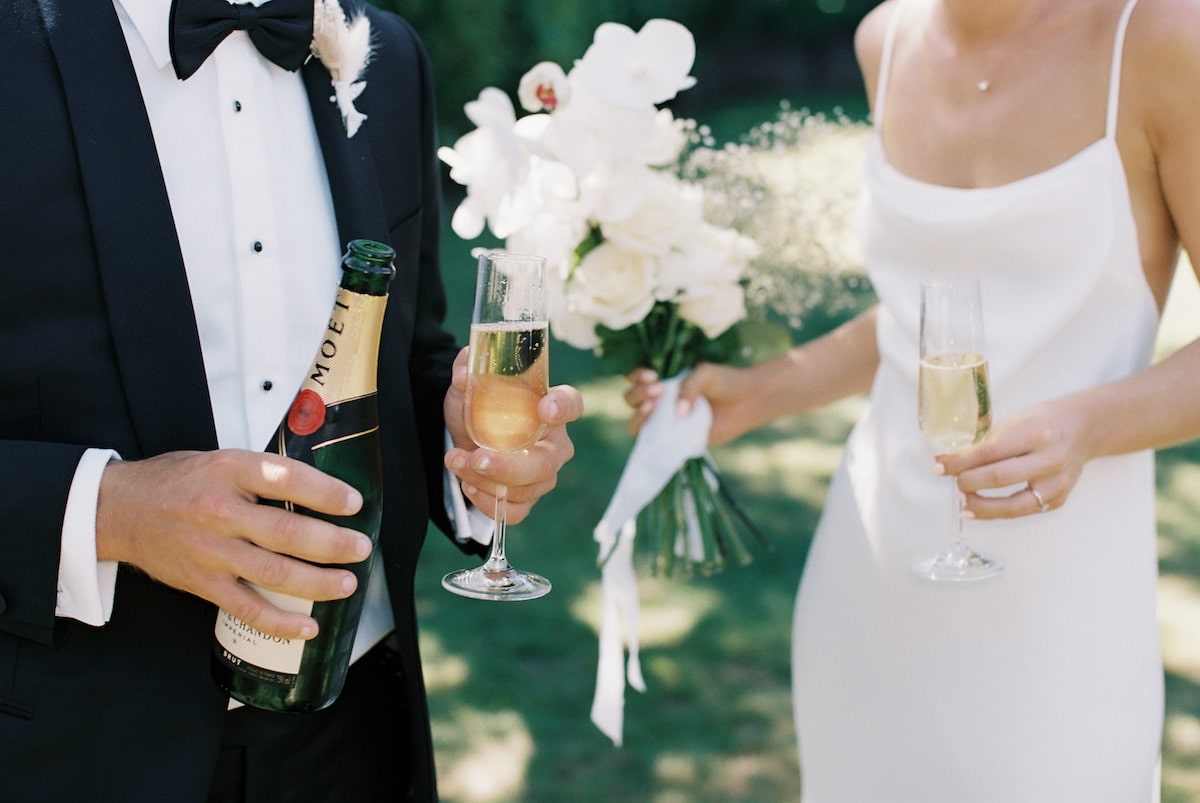 bride and groom holding champagne featuring bridal dress and groom's suit film photo Ana Galloway Photography