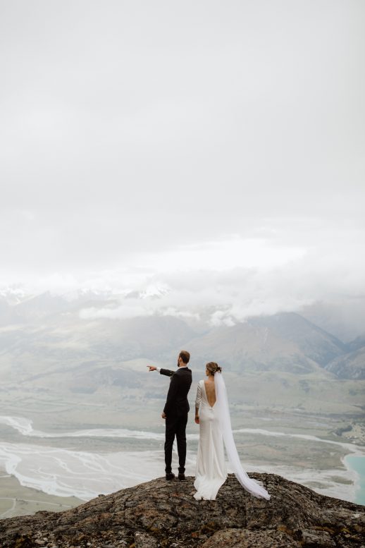 Bride and groom pointing in the distance on top of a mountain in Queenstown New Zealand Elopement Ana Galloway Photography