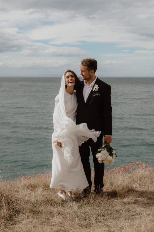 Bride and Groom happily waiting at the side of the beach with the cold breeze passing by them Ana Galloway Photography