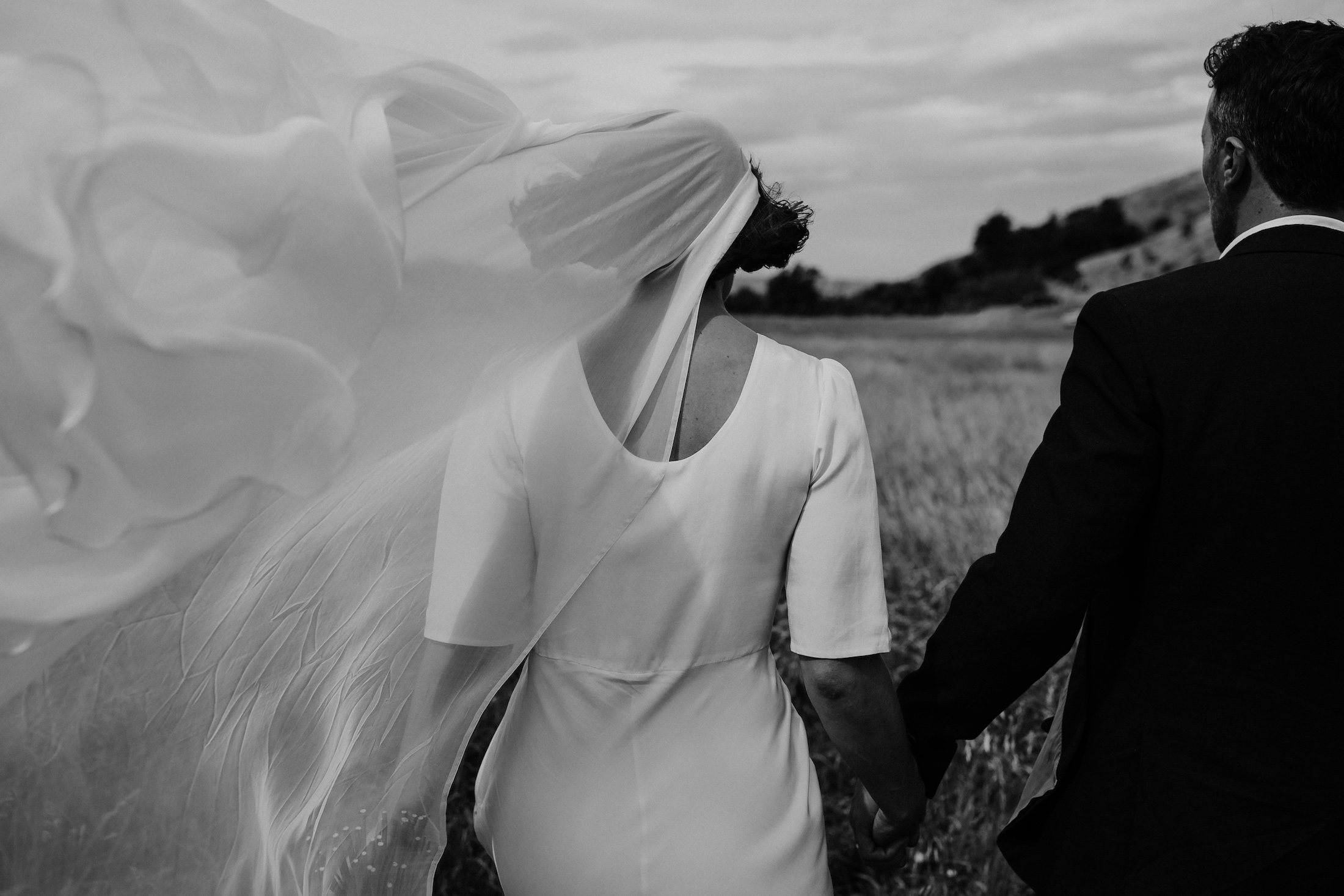 Bride and Groom walking in the grassy field with the cold breeze passing right through the veil Christchurch Wedding Ana Galloway Photography